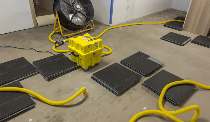 Dehumidifier, floor mats, and hoses for water damage restoration in a room