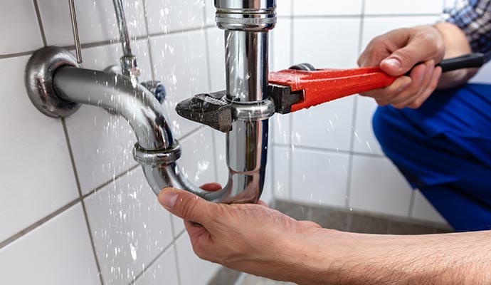 a person fixing a leaking pipe under a sink